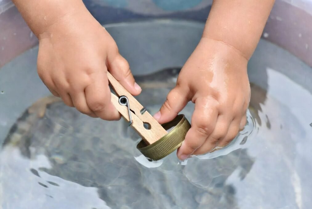 Adeus Telas: 20 Brincadeiras Educativas para Crianças de 3 a 7 Anos Fazerem em Casa 4 Close-up de mãos infantis a treinar o movimento de pinça com pregador e tampas.